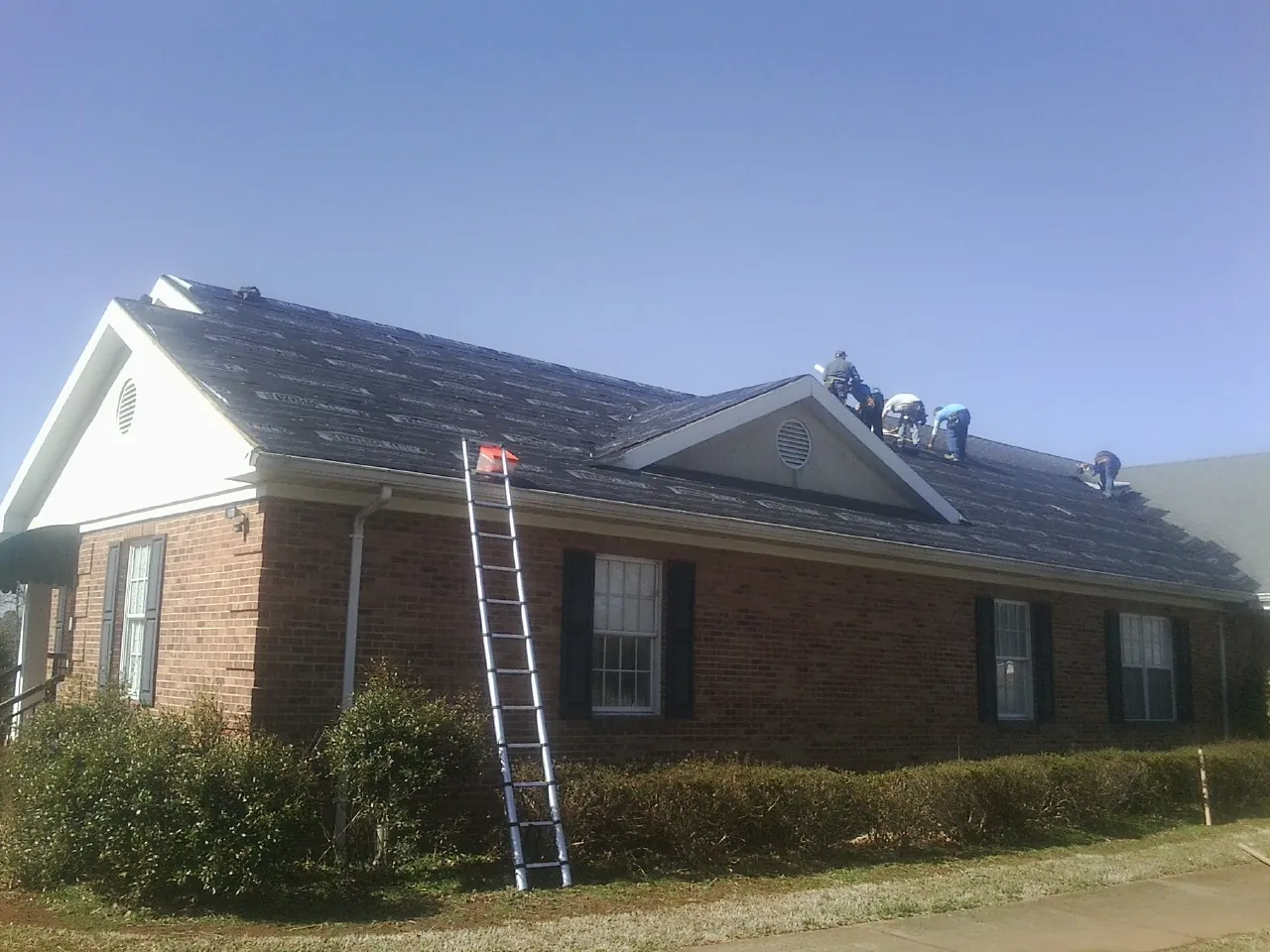 Crew tearing shingles off a brick ranch roof with a ladder set — Emergency Roof Repair work by our crew in San Bernardino