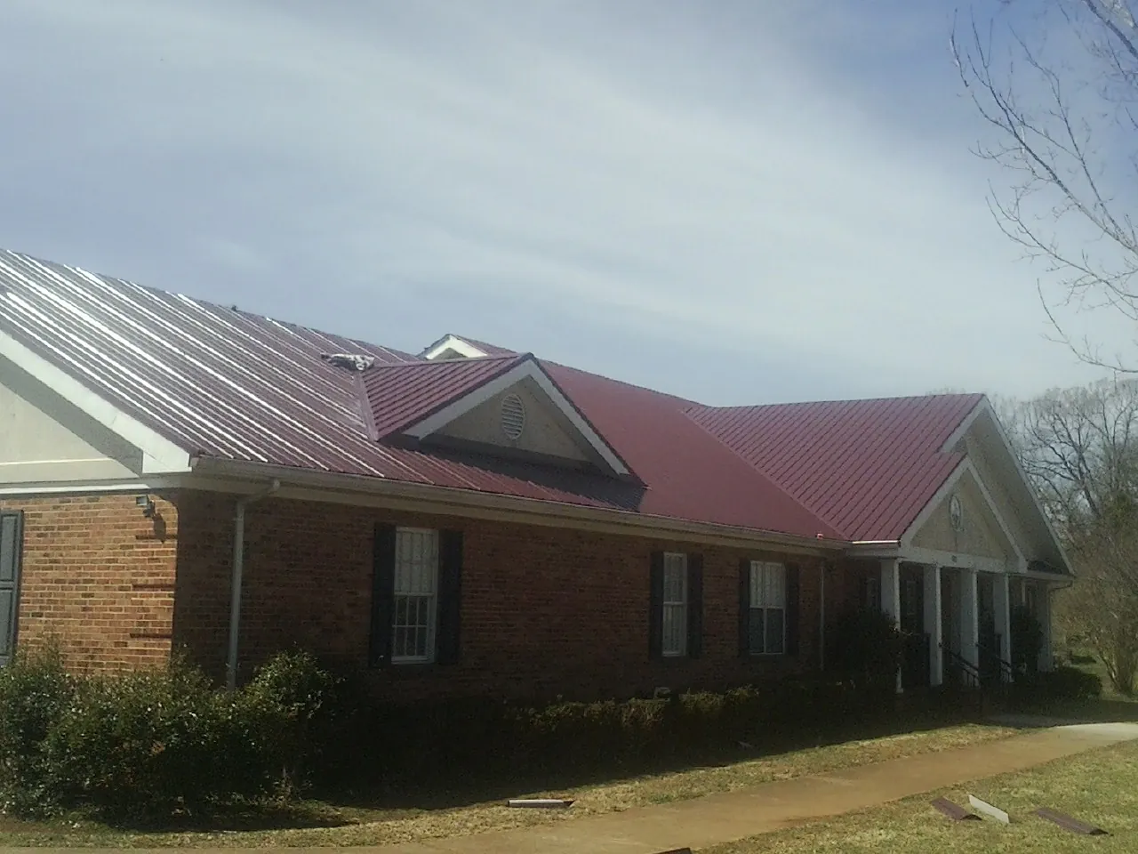 Red metal roof with gabled entries on a long brick building, from a Hail Damage Roof Repair job in San Bernardino