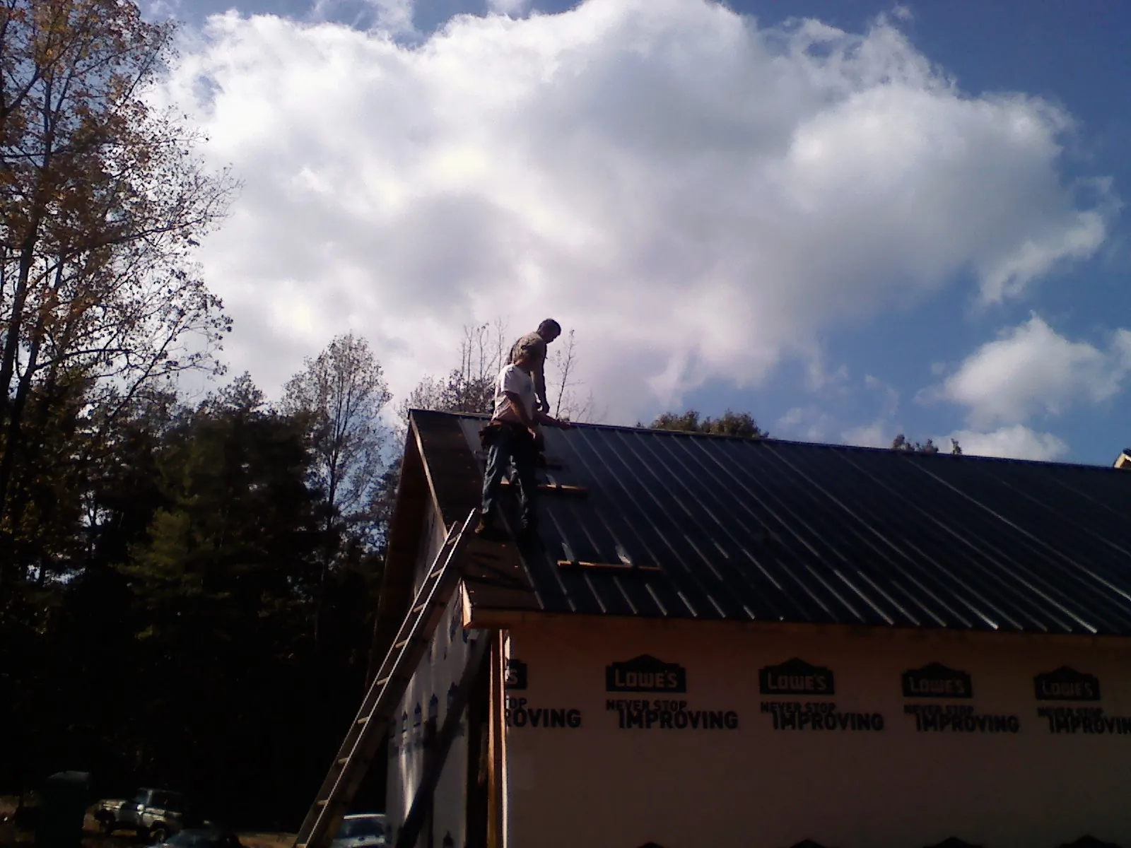 Roofer fastening dark metal panels high against a cloudy sky, from a Roof Inspection job in San Bernardino