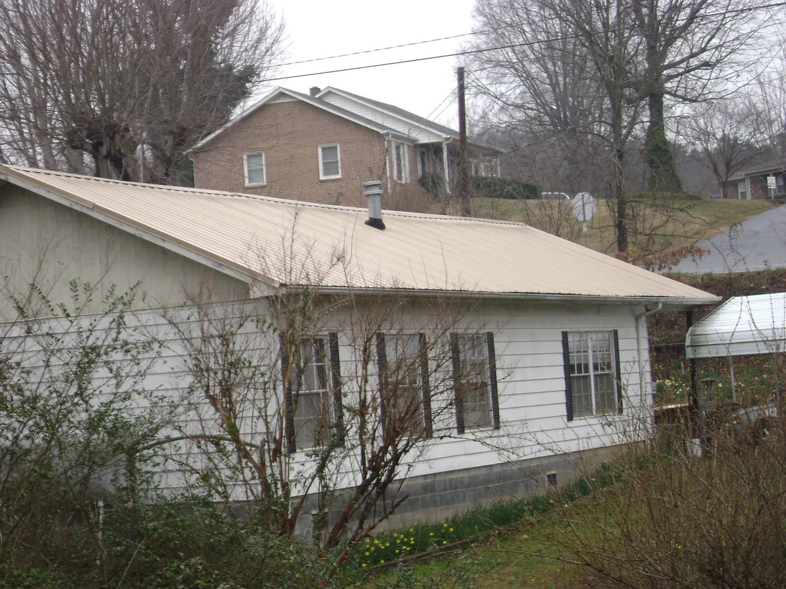 Tan metal roof on a white sided house set into a hillside — Commercial Roofing by Roofing Brothers in San Bernardino