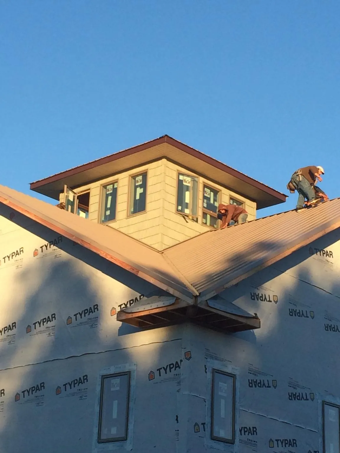 Roofers working around a rooftop cupola on a new metal roof at sunset — Roof Waterproofing in San Bernardino by Roofing Brothers